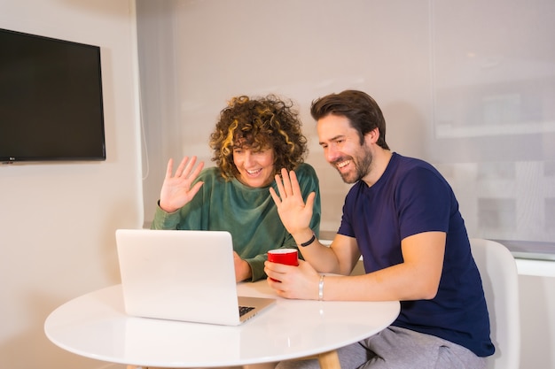 Lifestyle, a young Caucasian couple in pajamas having breakfast in the kitchen, making a family video call on the computer