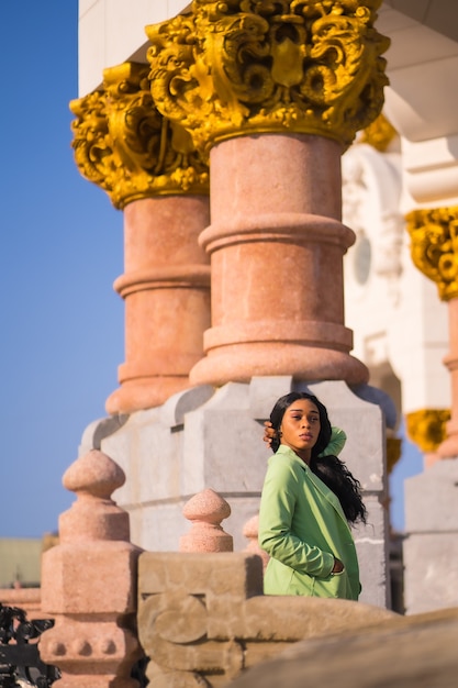 Lifestyle of a young girl of black african ethnicity with a beautiful green suit. tourist perched on the columns of the river looking to the left