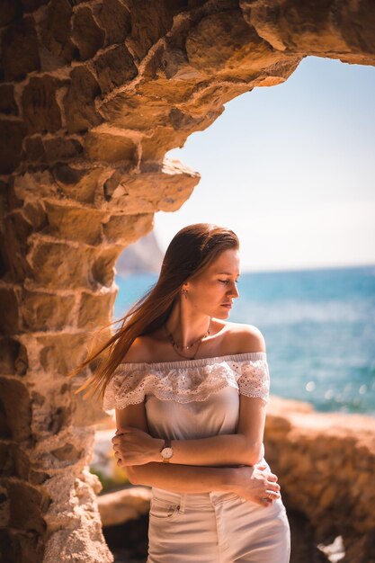 Lifestyle of a young pretty redhaired Caucasian woman dressed in white by the sea