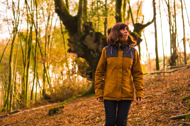 Lifestyle a young woman in a yellow jacket walking backwards along a forest