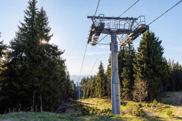 Lift with cable passes between spruce forest on peak against backdrop of mountain ranges of Rhodope Mountains