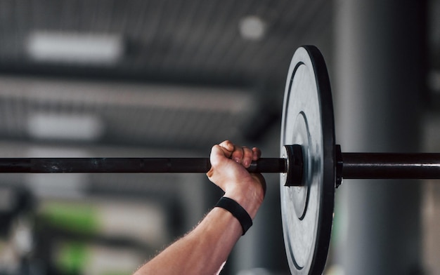 Bilanciere di sollevamento il giovane uomo sportivo e forte in abbigliamento nero ha una giornata di allenamento in palestra