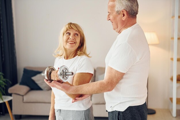 Lifting dumbbell Senior man and woman is together at home