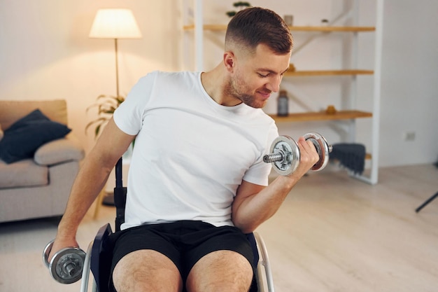 Lifting dumbbells Disabled man in wheelchair is at home