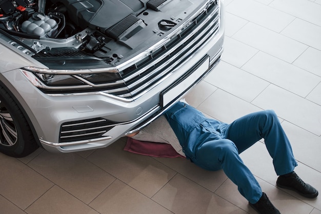 Foto liggend op de roze gekleurde handdoek. man in blauw uniform werkt met kapotte auto. reparaties maken.