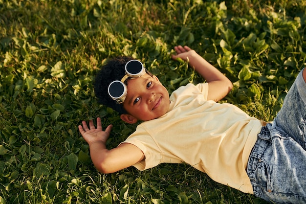 Liggend op het gras Afro-Amerikaanse jongen veel plezier in het veld op zomerdag