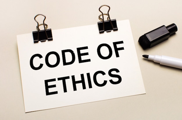 On a light background, a black open marker and on black clips a white sheet of paper with the text CODE OF ETHICS