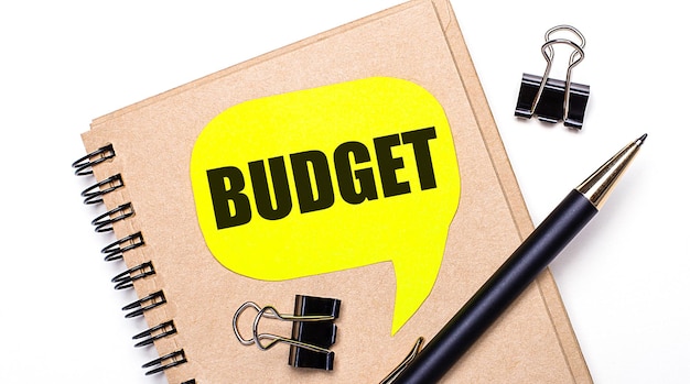 Foto su fondo chiaro, un quaderno marrone, una penna nera e graffette e un cartellino giallo con la scritta budget. concetto di affari.
