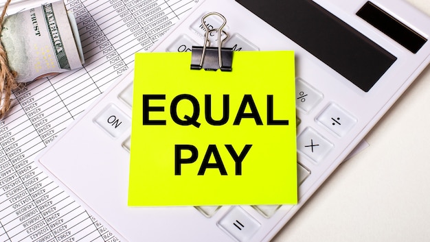 明るい背景-現金、白い電卓、黒いペーパークリップの下にある黄色のステッカーと「EQUALPAY」というテキスト。ビジネスコンセプト