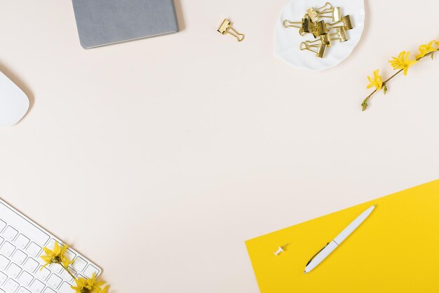 Photo on a light background flat lay with a yellow flower a notepad keyboard and paper clips a female floral desktop the concept of a stylish spring or summer morning top view and copy space