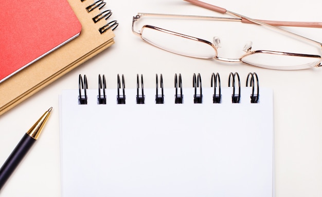 On a light background - glasses in gold frames, craft and red notebooks and a white blank notebook with a place to insert text. Business concept