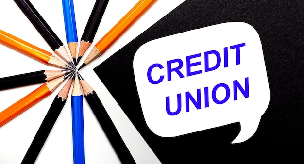 On a light background, multi-colored pencils and on a black background a white card with the text CREDIT UNION