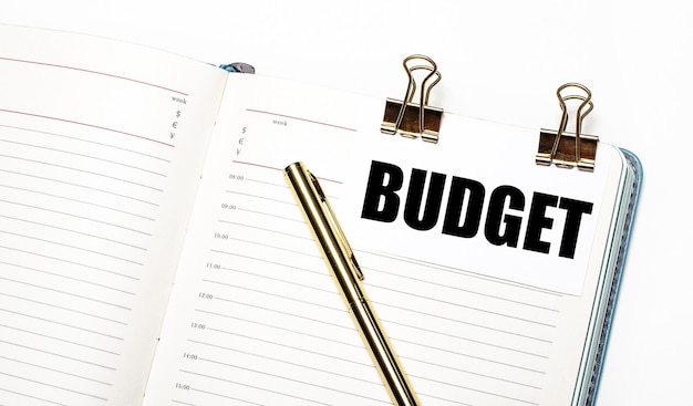 on a light background, an open notebook, a sheet of paper with gold clips and the text budget and a gold pen. view from above. business concept