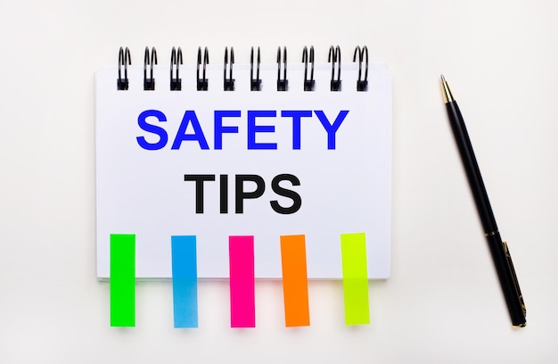 On a light background, a pen, a notebook with the text SAFETY TIPS and bright stickers.