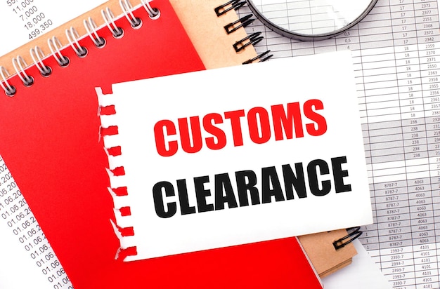 On a light background reports a magnifying glass brown and red notepads and a white notepad with the text CUSTOMS CLEARANCE Business concept