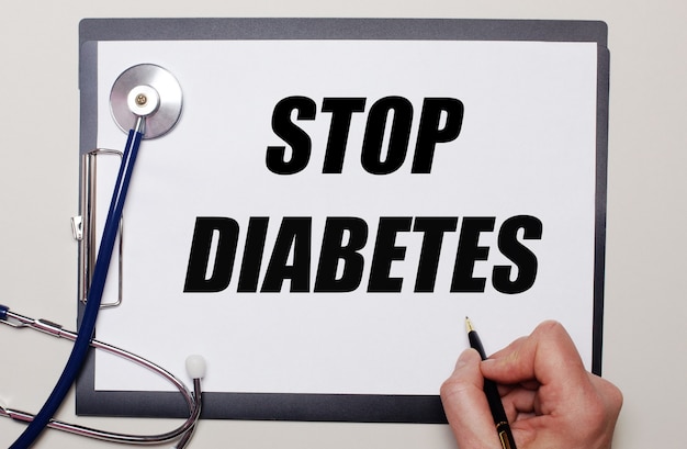 On a light background, a stethoscope and a sheet of paper, on which a man writes STOP DIABETES. Medical concept