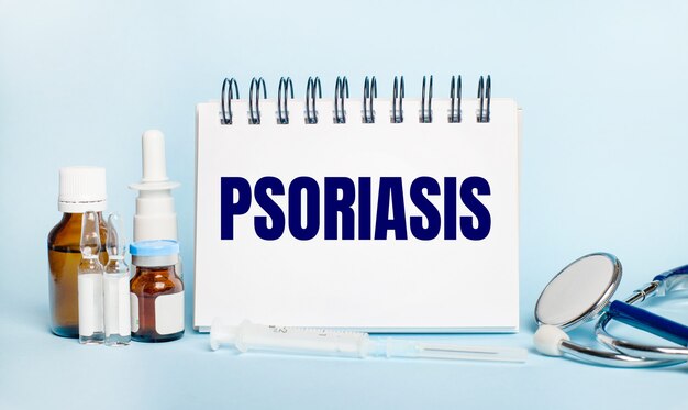 On a light background, a syringe, a stethoscope, vials of medicine, an ampoule and a white notepad with the text PSORIASIS