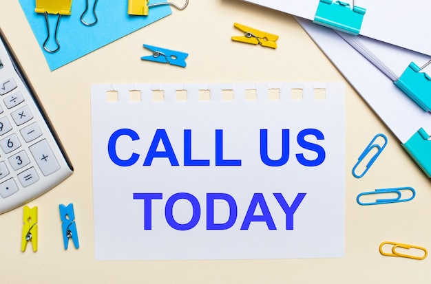 On a light background, there are stacks of documents, a white calculator, yellow and blue paper clips and clothespins, and a notebook with the text CALL US TODAY