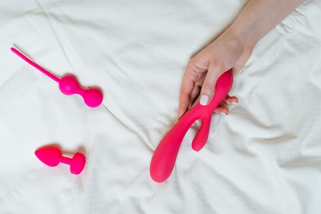 Light background with different sex toys a vibrator in a womans hands