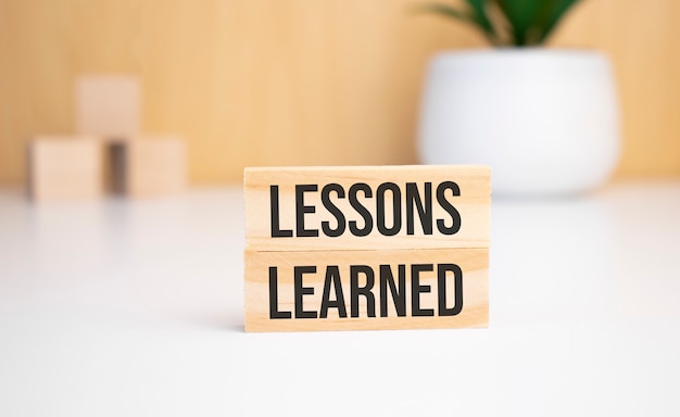 On a light background, wooden cubes and a wooden block with the text LESSONS LEARNED. View from above