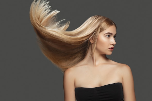 Light Beautiful model with long smooth flying blonde hair on dark grey studio background