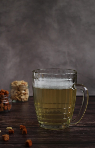 Photo light beer in a glass mug with crackers and peanuts on a dark background