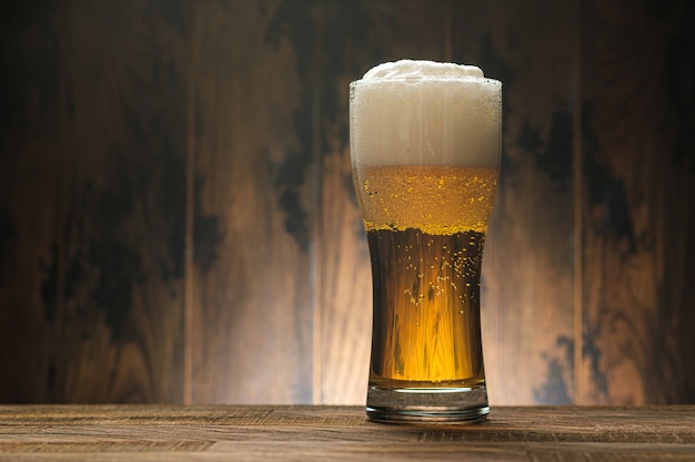 Light beer in glass with foam on wooden