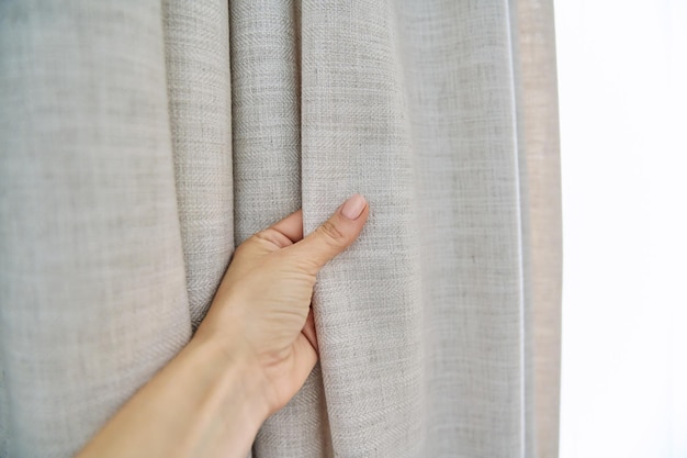 Light beige sand linen natural curtains on window closeup of hand touching curtains