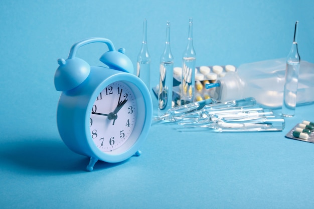 Light blue alarm clock and medicines on a blue background, expiration date of drugs concept