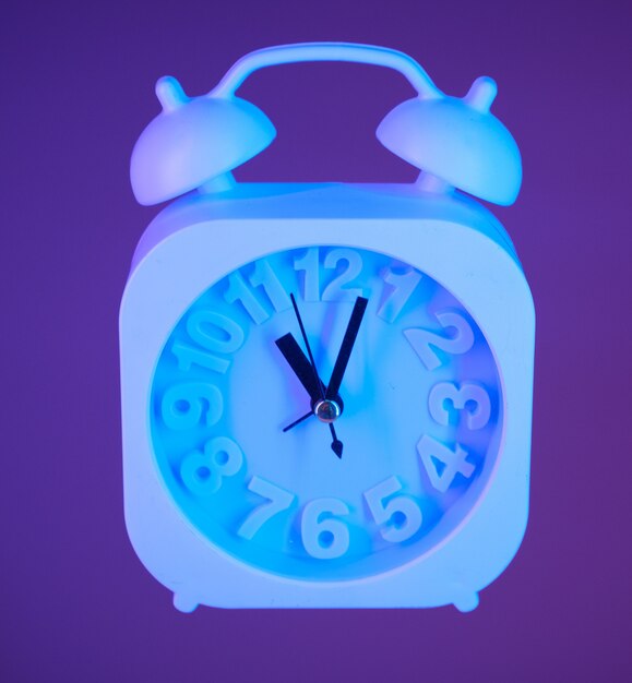 Light blue alarm clock suspended in air on a bright purple background