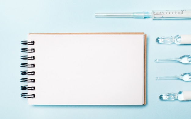 On a light blue background ampoules, a syringe and a blank notebook.