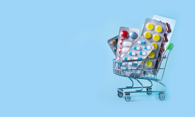 Su uno sfondo azzurro un carrello della spesa con le pillole concetto medico spazio di copia
