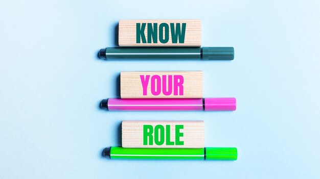 On a light blue background, there are three multi-colored felt-tip pens and wooden blocks with the KNOW YOUR ROLE text.