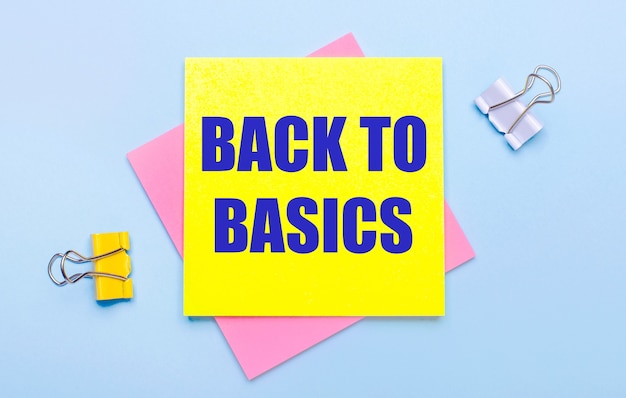 On a light blue background, there are yellow and white paper clips, pink and yellow sticky notes with the text BACK TO BASICS