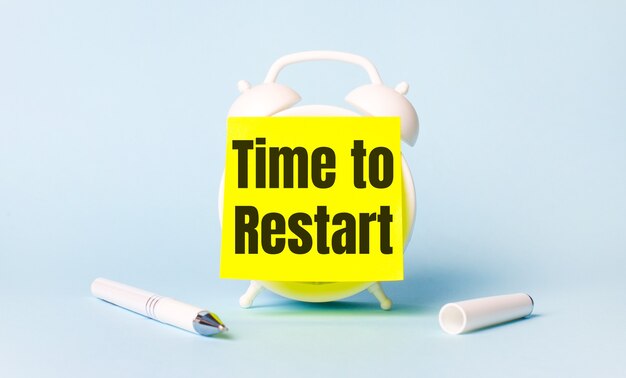 On a light blue background - a white handle and an alarm clock with a bright yellow sticker glued to it with the text TIME TO RESTART