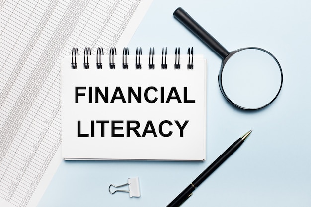 하늘색 표면에 FINANCIAL LITERACY라는 텍스트가있는 보고서, 돋보기, 펜 및 노트북