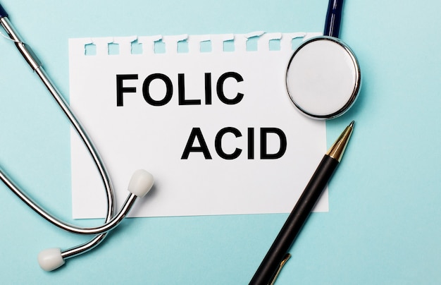 On a light blue surface, a stethoscope, a pen and a sheet of paper with the inscription FOLIC ACID