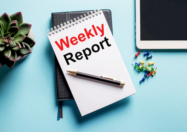 On a light blue surface, there is a potted plant, a tablet and a weekly with the text weekly report