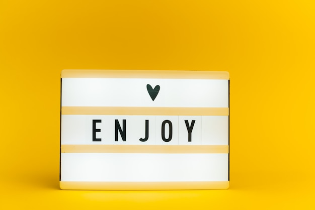 light box with text, ENJOY, on yellow wall