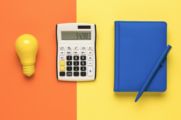 Лампочка, калькулятор и блокнот на двухцветном фоне.
