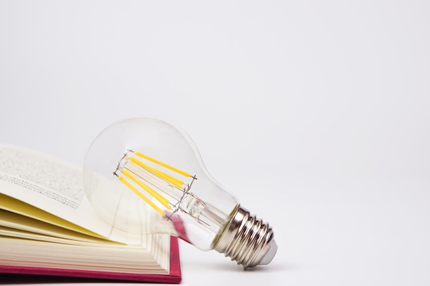 Фото Лампочка, светящаяся книгой на белом фоне концепция знаний, новые идеи и творчество