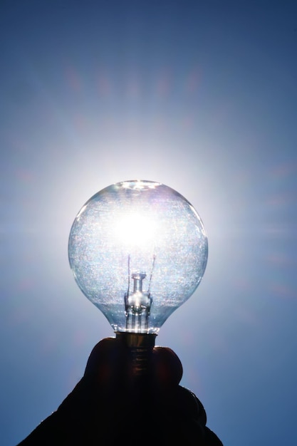 Light bulb in hand against the sky with a sun