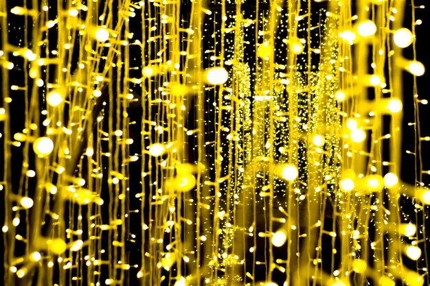 Foto lampadina appesa a un lampadario, che illumina un piccolo, bellissimo bokeh oro giallo su sfondo nero.