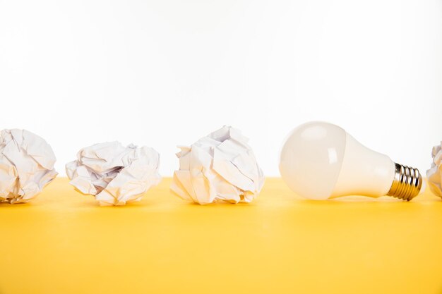 Light bulb near crumpled paper on yellow surface isolated on white