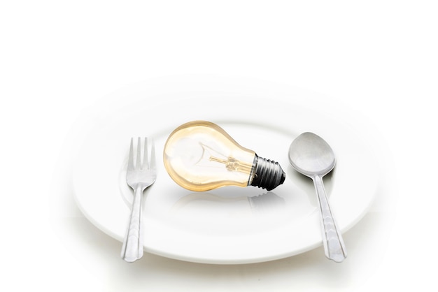 Лампочка в тарелке и вилкой и ложкой, изолированных на белом