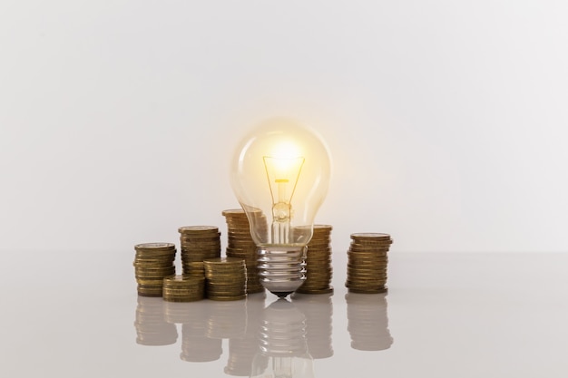 Light bulb with coin piles on white table