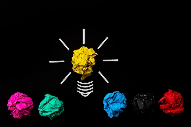 Light bulb with crumpled colorful paper on black background.