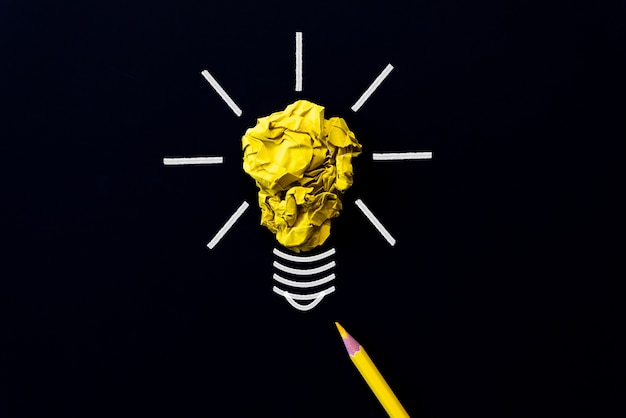 Light bulb with crumpled colorful paper and yellow pencil on black background.