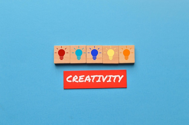 Light bulb on wooden blocks and the word CREATIVITY