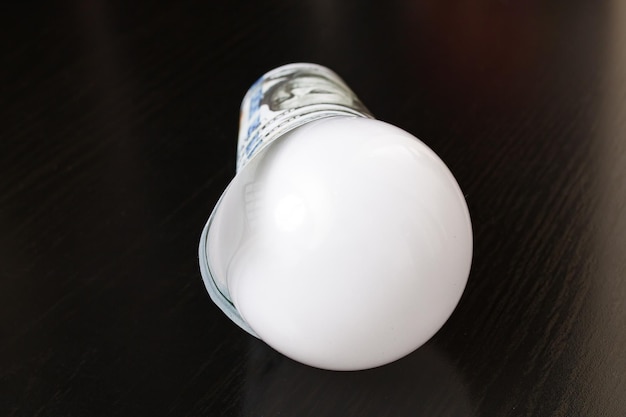 Photo light bulb wrapped in dollars on wooden table